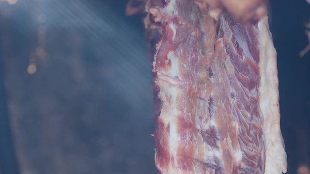 Ham and bacon hanging and drying in smokehouse on traditional way on blue smoke.  The sunrays pierce through the blue smoke.