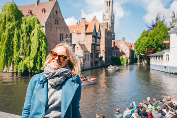 Naklejka premium A beautiful young girl sits on the background of a famous tourist spot with a canal in Bruges, Belgium