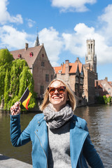 A young woman with the flag of Belgium in her hands is enjoying the view of the canals in the historical center of Bruges.
