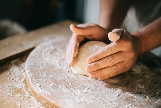 Man kneading and baking homemade pizza dough in the kitchen. Closeup on baker's hands preparing loaf of bread.