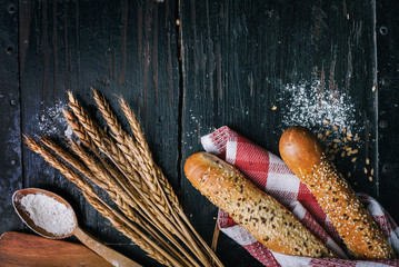 Fresh french baguette bread, organic flour and wholegrain wheat on dark vintage wooden board form...