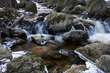 Fototapeta premium Frozen brook and waterfalls with icy pieces. Winter mountain nature in forest.