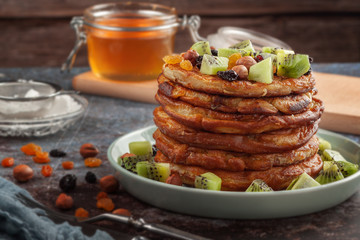 On the table is a dish with pancakes, honey, kiwi, nuts and raisins.