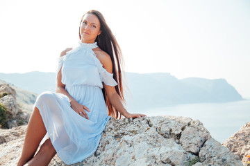 A beautiful woman with long hair in a dress looks out over the sea from a cliff