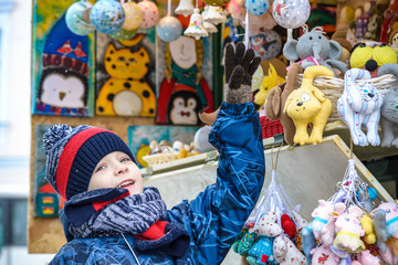 Naklejka premium Little cute kid boy selecting decoration on Christmas market. Beautiful child shopping for toys and decorative ornaments. Traditional winter holiday event