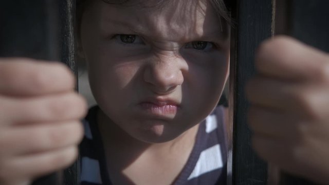 Child by metal bar. Portrait of an angry little girl behind an iron fence.
