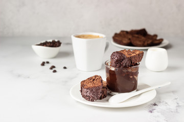 Traditional Italian homemade biscotti cookies or cantuccini with chocolate and a cup of coffee on a light grey background.