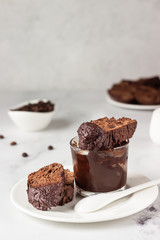 Traditional Italian homemade biscotti cookies or cantuccini with chocolate and a cup of coffee on a light grey background.
