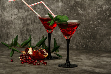 Red cocktail with pomegranate juice in a martini glass with ice on a gray background. Red cocktail with martini and pomegranate juice on a gray stone background.