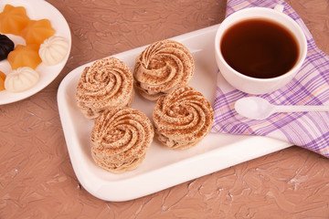 Food, dessert, handmade marshmallows. On a white plate are delicious, sprinkled with cinnamon and chocolate four marshmallows, a Cup of tea and a variety of marmalade. Warm brown background.