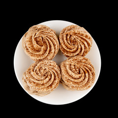 Four handmade marshmallows, sprinkled with cinnamon and chocolate, lie on a white plate. The view from the top, highlighted on a black background.