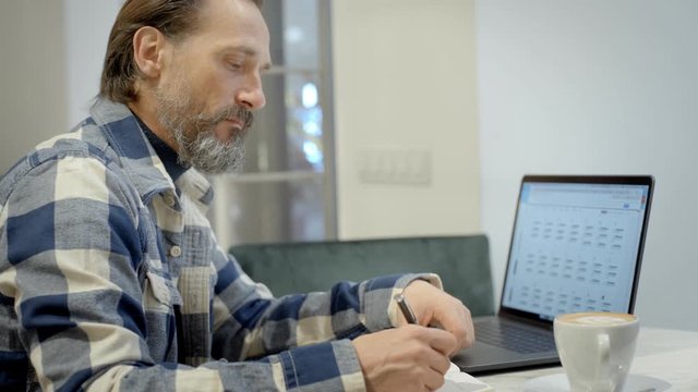 Adult handsome man works in cafe on laptop