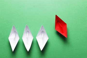 Flat lay of white paper ships and red paper boat on green background. Not like that. Individuality....
