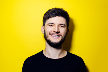 Fototapeta premium Studio portrait of young smiling man wearing black on yellow background.