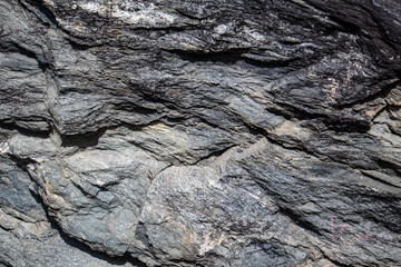 Grey black granite stone on natural wall in mountains. Close up gray texture, rough surface material. For design, web