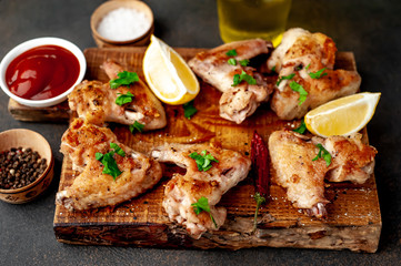 grilled chicken wings on a cutting board with spices and herbs on a stone background