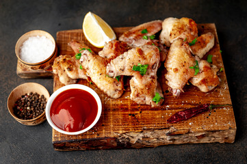 grilled chicken wings on a cutting board with spices and herbs on a stone background