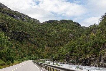 Mountains in Norway road near rocky river epic scenic sky, way, clouds view. Traveling by car, driving nature tourism. Dramatic skyscape northern scandinavian sky