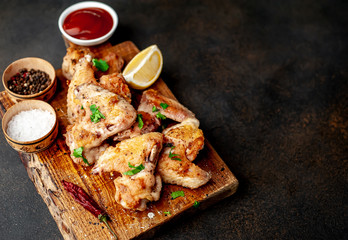 grilled chicken wings on a cutting board with spices and herbs on a stone background