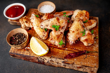 grilled chicken wings on a cutting board with spices and herbs on a stone background