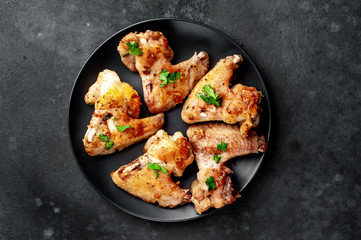 grilled chicken wings on a black plate with spices and herbs on a stone background with copy space for your text