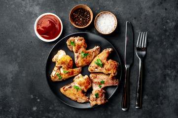 grilled chicken wings on a black plate with spices and herbs on a stone background with copy space for your text
