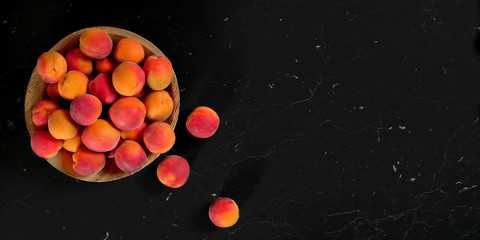 Fototapeta na wymiar Small bowl with apricots, some of them scattered near on black marble like table - view from above, space for text right side