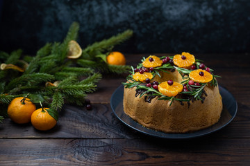 Tangerine ring cake decorated with sliced mandarines, cranberries and rosemary on dark blue background with copy space.