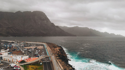 Aerial view of the promenade and coastal stones in the port city of Agaete. Giant misty rocks hanging over the dark Atlantic Ocean