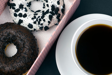 Chocolate donuts and coffee. Two beautiful tasty donuts in a pink box and a cup of aromatic hot coffee close-up