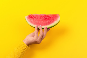 hand holds watermelon slice over yellow background.  Summertime concept.