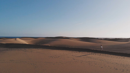 Fototapeta na wymiar Aerial view - an attractive girl walks along the sand in the rays of the setting sun, Maspalomas, Gran Canaria