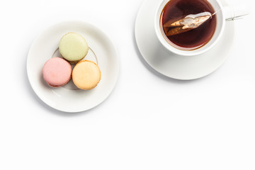 three delicious macaroons on a plate and a cup of tea on white background