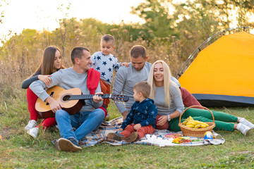 travel, tourism, hike, picnic and people concept - group of happy friends with tent and drinks playing guitar at camping