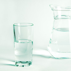 Pure clear water in a glass glass and glass jug stands on a white background