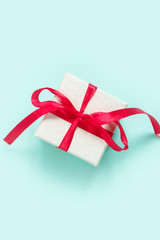 Christmas flat lay on top, New Year gift in a box with a red ribbon on a neo mint background, festive decor, copy space