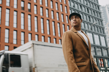 View of young handsome arabian man stand outside and pose. Truck driving behind him. Guy look...