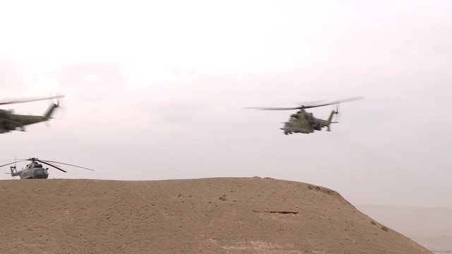 Combat link military helicopters flying over the desert between the mountains, attacking from the air of the enemy.