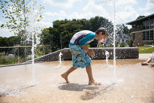 Boy With Face Splashing In Water At Splash Pad Park