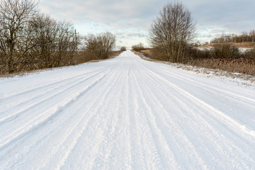 Obraz premium Rural road in the forest covered with snow. Travel on a snowy road on a winter day through the forest
