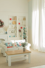 The interior of the Christmas room with a large window, a white sofa with pillows at the coffee table.