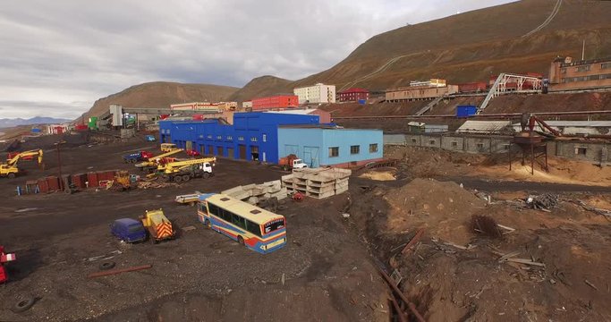 Svalbard. Barentsburg. The aerial view over the arctic settlement. Modern and outdated buildings, cars and machinery against the backdrop of a harsh Arctic landscape under the cloudy sky. 4K