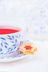 Pink fruit tea and homemade cookie star with jam on a white wooden background