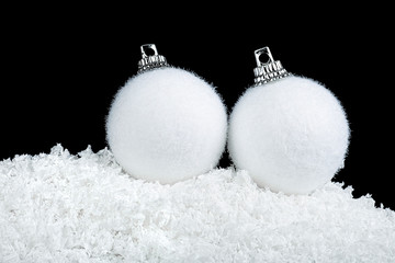 Two white christmas balls in snow on a black background