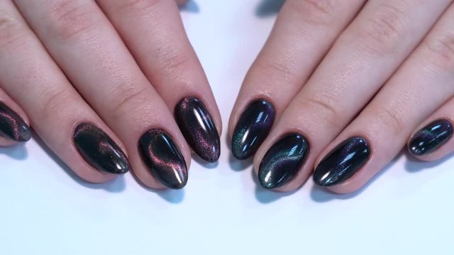 Closeup top view of professional colorful glossy brilliant holiday manicure at fingers of young woman. Modern trendy shiny amazing cat eye effect nail design. Real time 4k video footage.