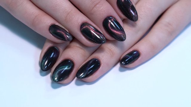 Closeup top view of professional colorful glossy brilliant holiday manicure at finger of young woman. Modern trendy shiny amazing cat eye effect nail design. Real time 4k video footage.