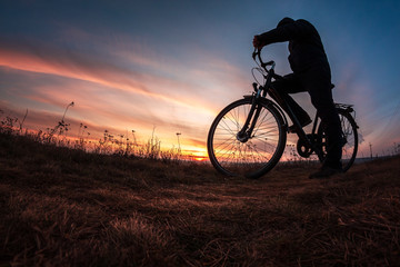 Fototapeta na wymiar man with bicycle on the mountain looks at sunset