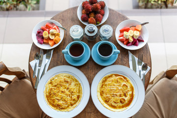 Top view, table setting. Balinese tropical breakfast of fruit, coffee and scrambled eggs and banana pancake for two. on the street near the pool