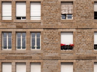 Facade of the stone wall with windows and red flower in the window.