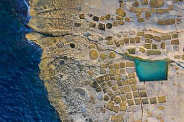 Salt pans on Gozo island. Blue sea and rocks. View from above, aerial. Malta country